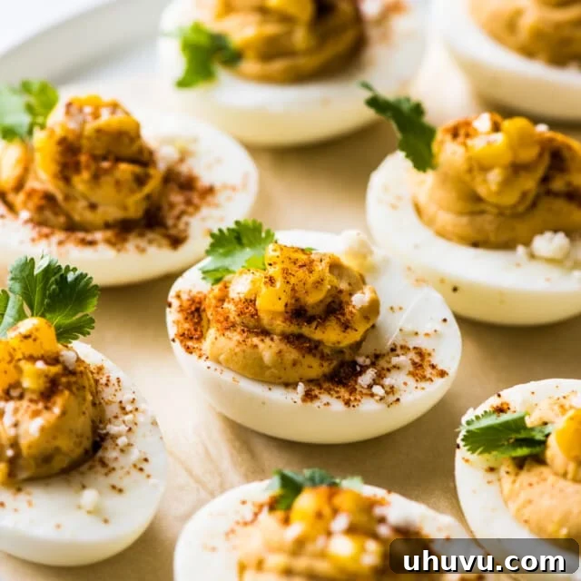 Mexican deviled eggs on a plate topped with corn, cilantro, chili powder, and cotija cheese.