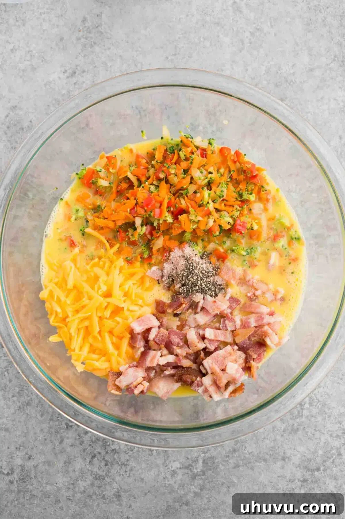 mixing eggs, sautéed vegetables, and bacon bits in a bowl