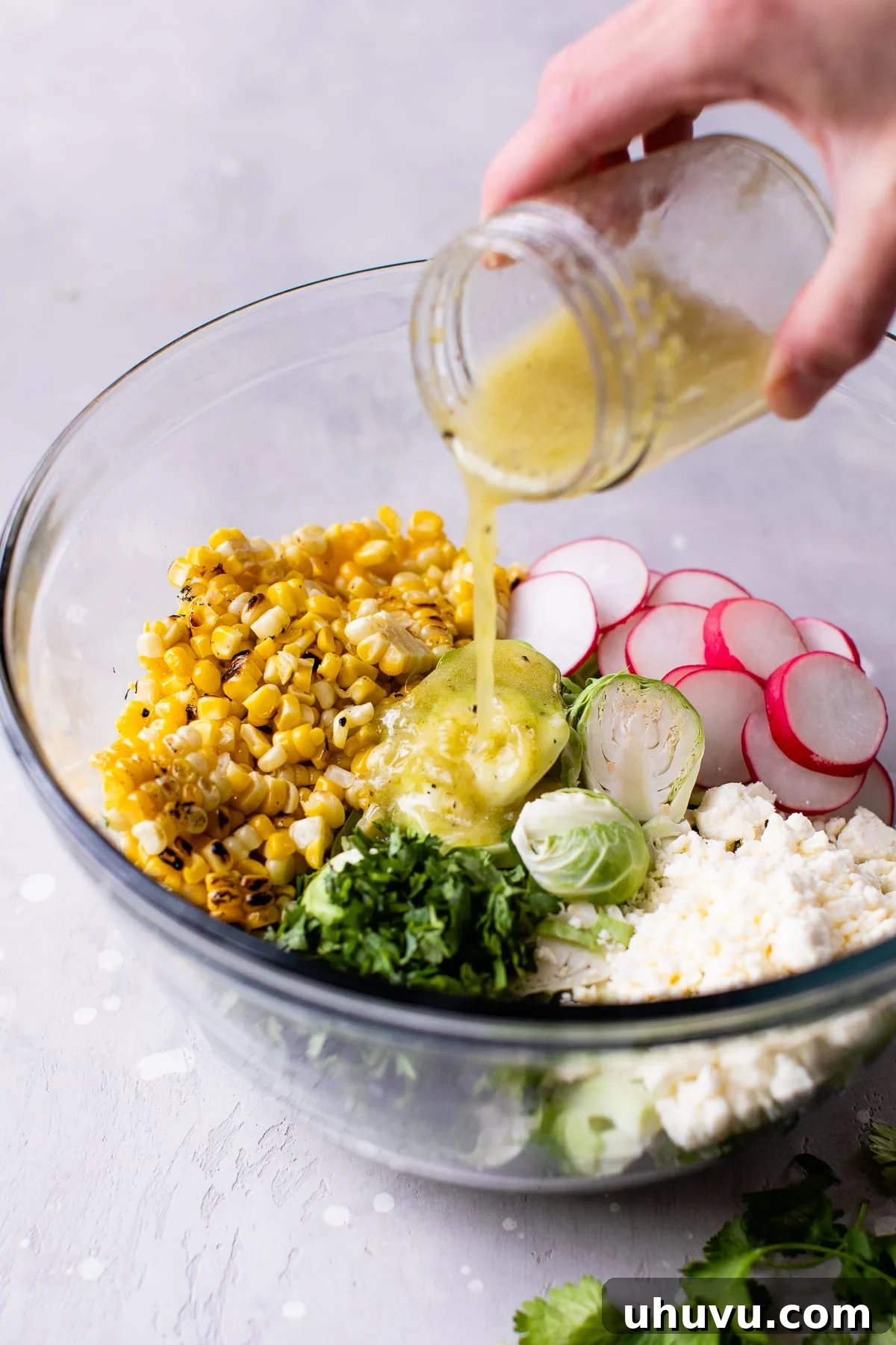 Zesty Mexican Brussels Sprout Salad 4 Dressing being poured over Mexican Brussels Sprouts Salad ingredients in a bowl, capturing the moment of flavor infusion.