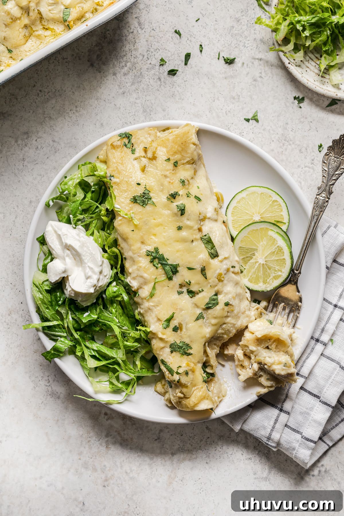 Creamy Chicken Enchiladas 5 A single white chicken enchilada on a plate, garnished with shredded lettuce, a dollop of sour cream, and fresh cilantro.