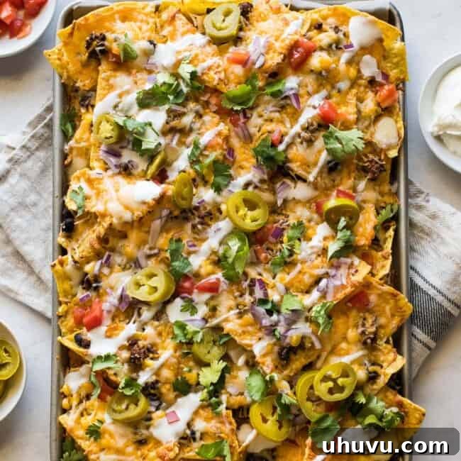 Sheet pan nachos topped with sour cream, pickled jalapenos, tomatoes, and cilantro.