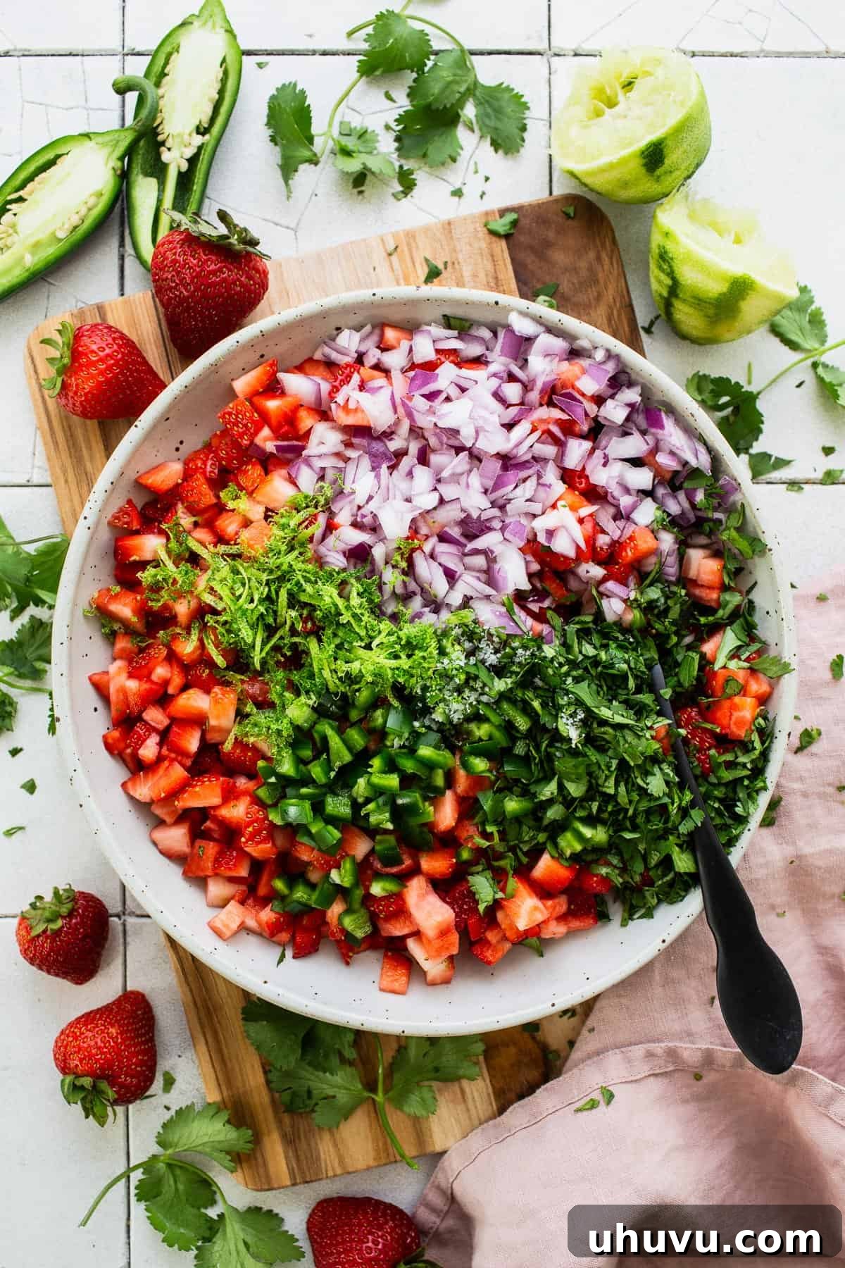 A close-up of finely chopped strawberries, diced red onion, and fresh cilantro leaves in a large glass mixing bowl, ready to be combined.