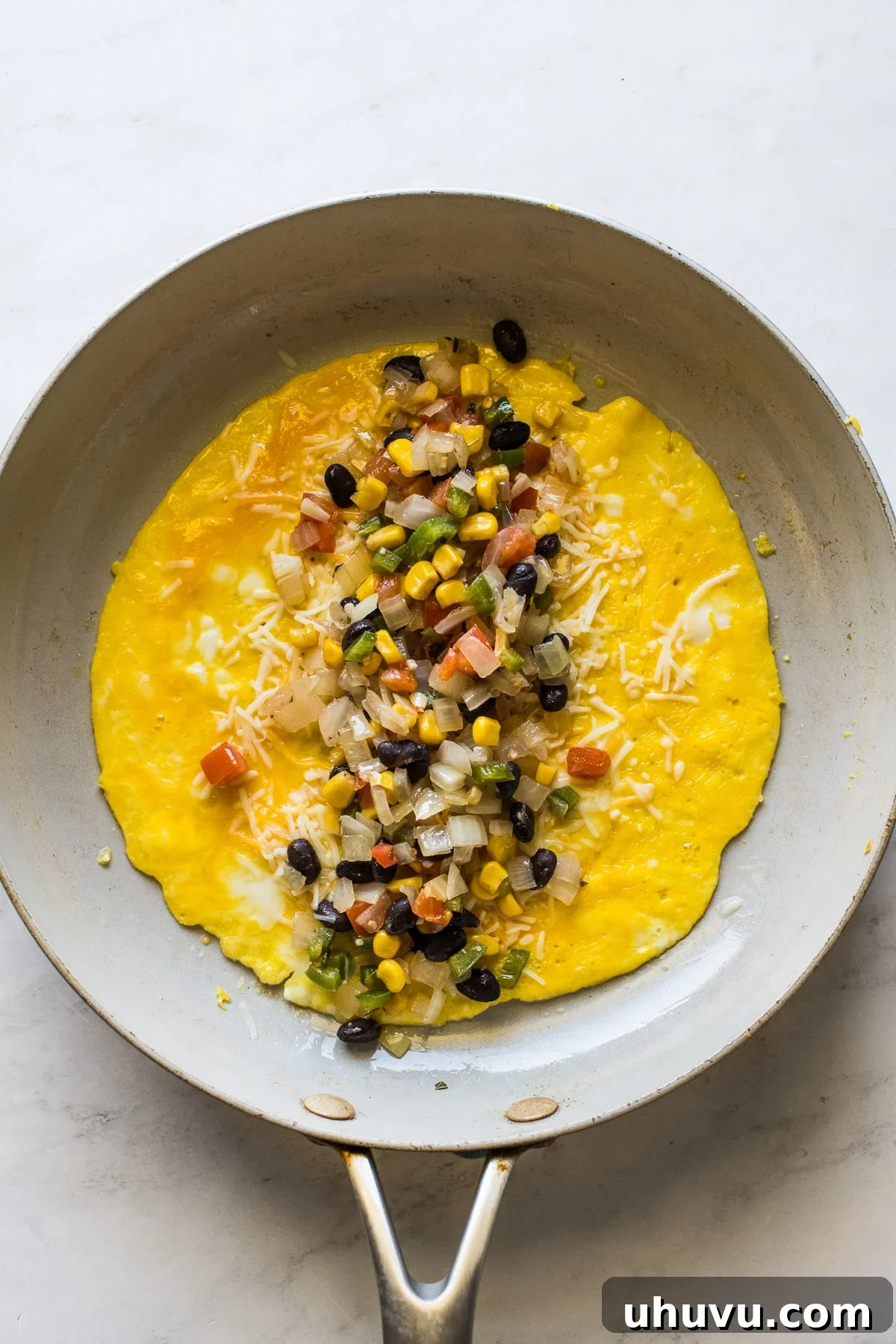 Fiesta Omelet 5 A perfectly cooked omelet in a non-stick skillet, generously filled with melted cheese and a vibrant mixture of beans, corn, onions, and peppers.