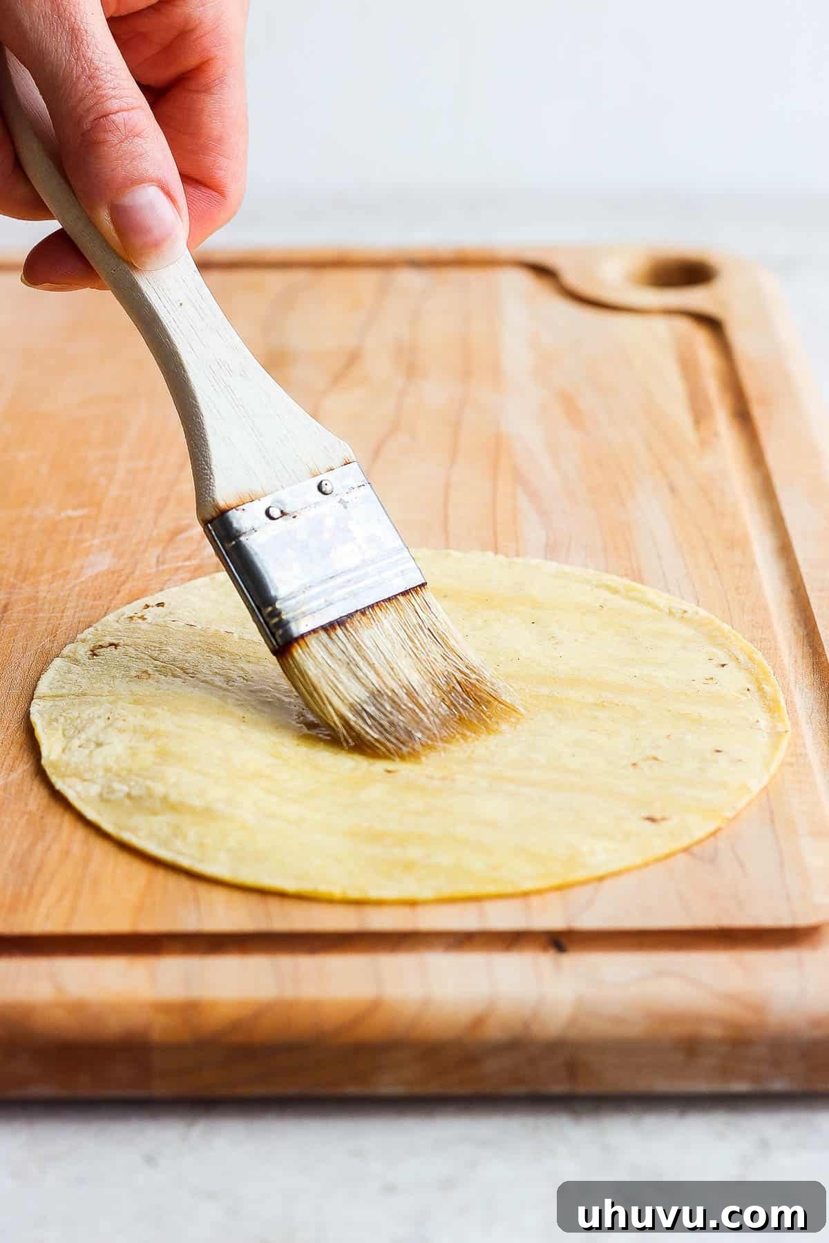 Brushing cooking oil on one side of a corn tortilla 