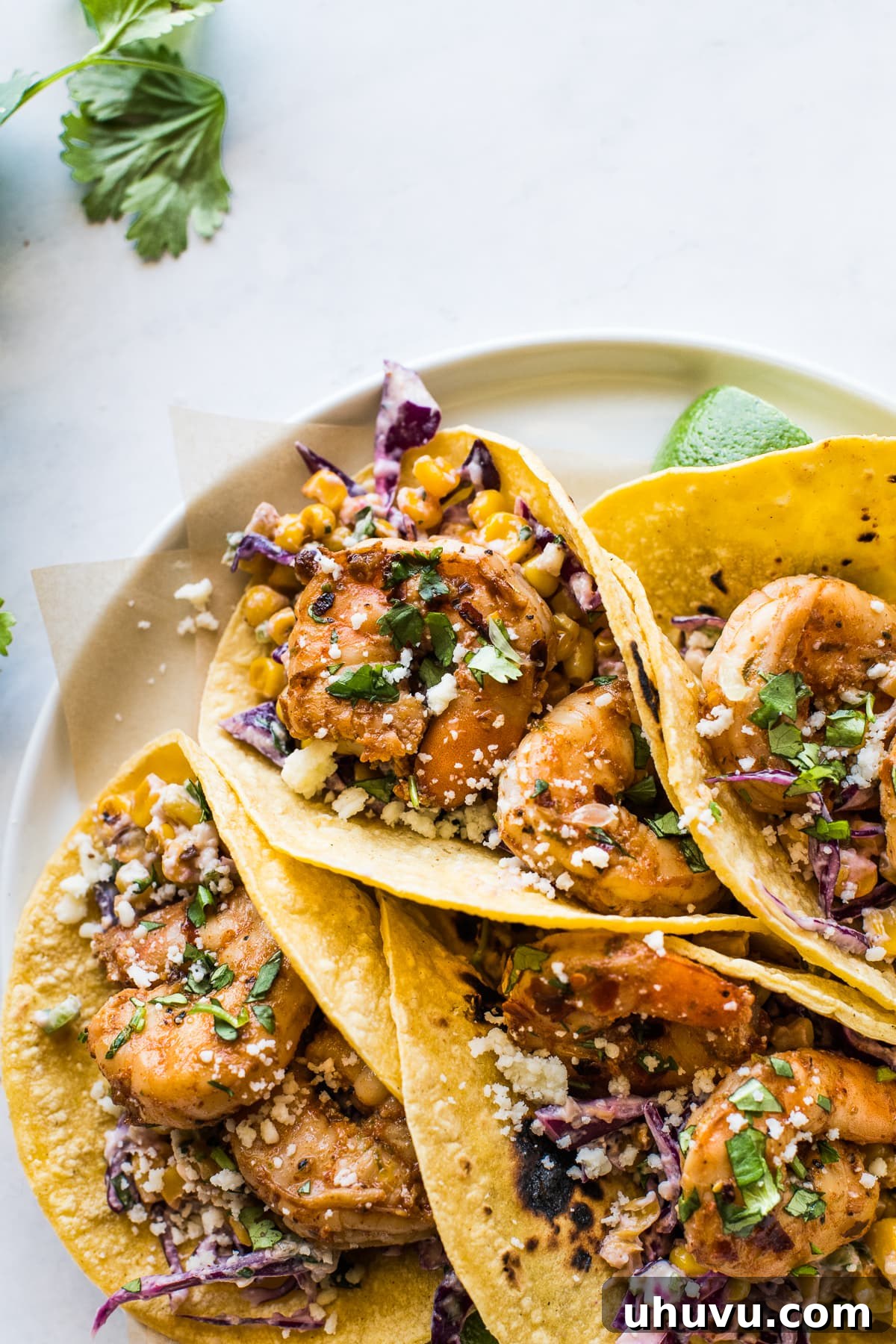 Chili-Lime Shrimp Tacos with Creamy Elote Slaw 6 Artfully arranged spicy shrimp tacos, generously topped with fresh cilantro and crumbled cotija cheese, promising a burst of Mexican-inspired flavor.