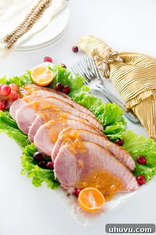 Slice of Orange Dijon Glazed Ham on a plate with fresh herbs.