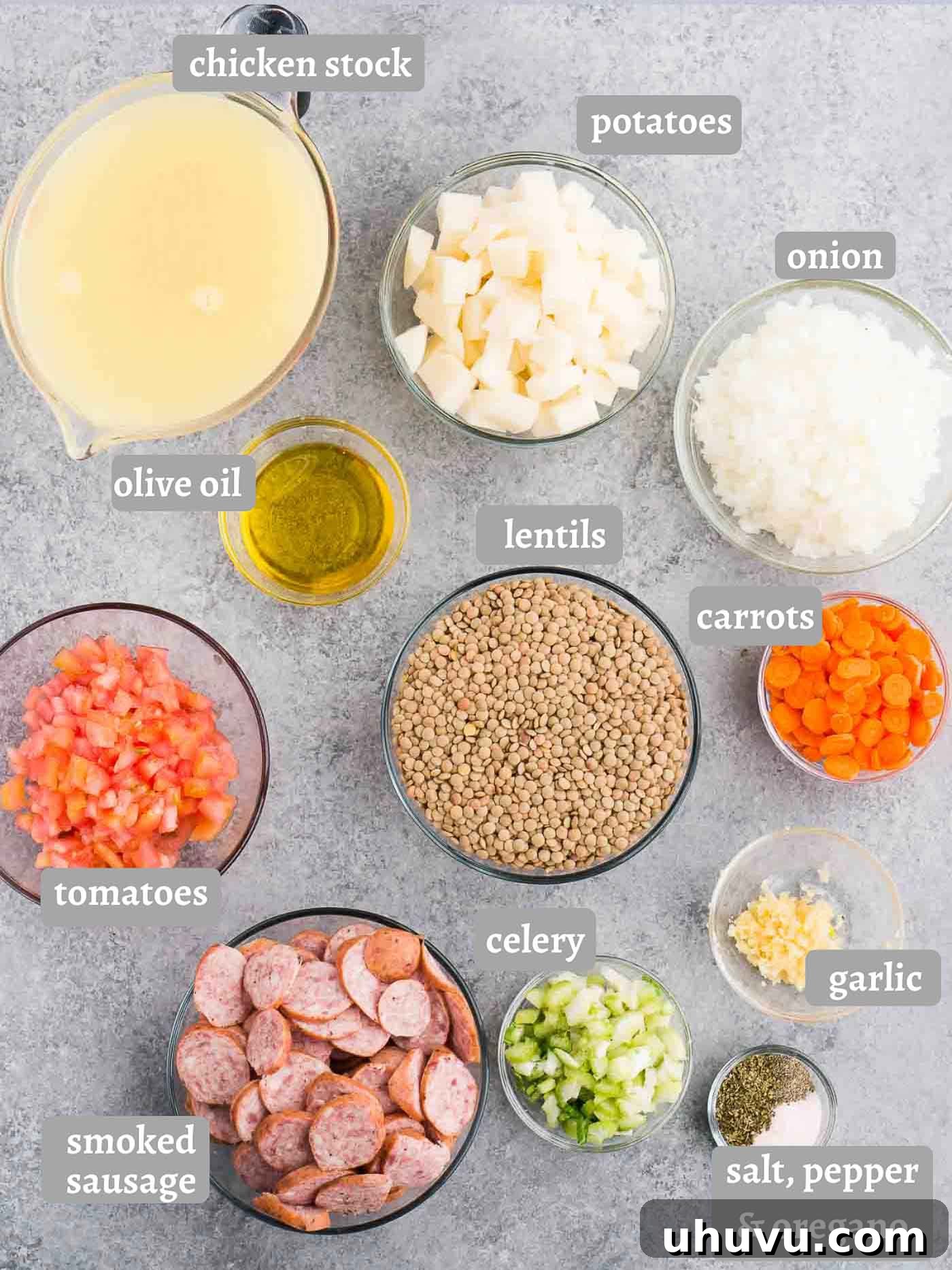 A flat lay image displaying all the fresh ingredients laid out for making lentil soup, including sausage, various vegetables, and spices.