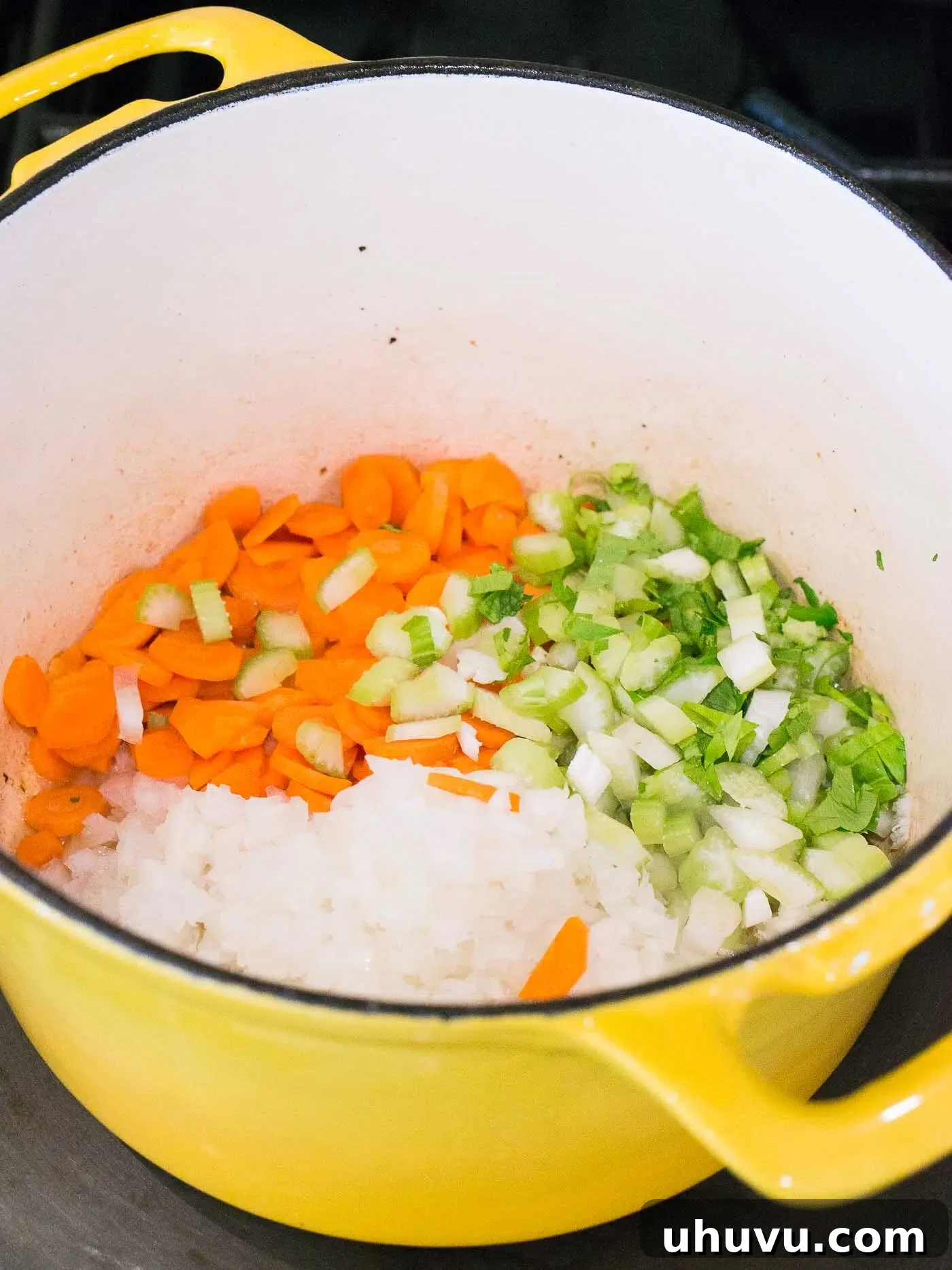 Chopped onions, carrots, and celery being sautéed in a pot, releasing their aromatic flavors.