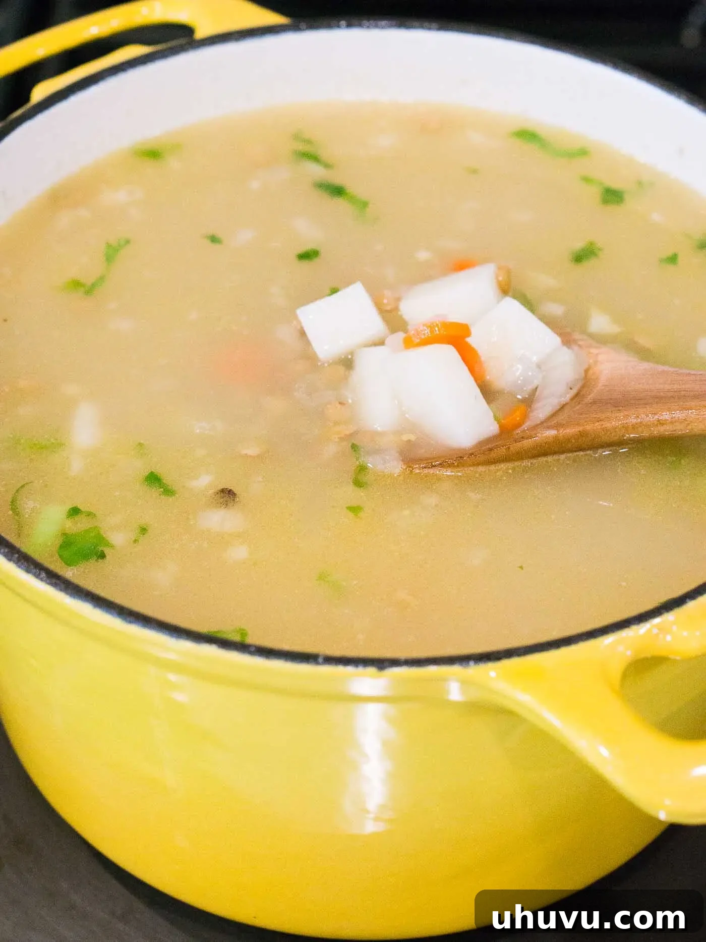 Lentil soup simmering in a large pot with broth, lentils, and potatoes, cooking until tender.