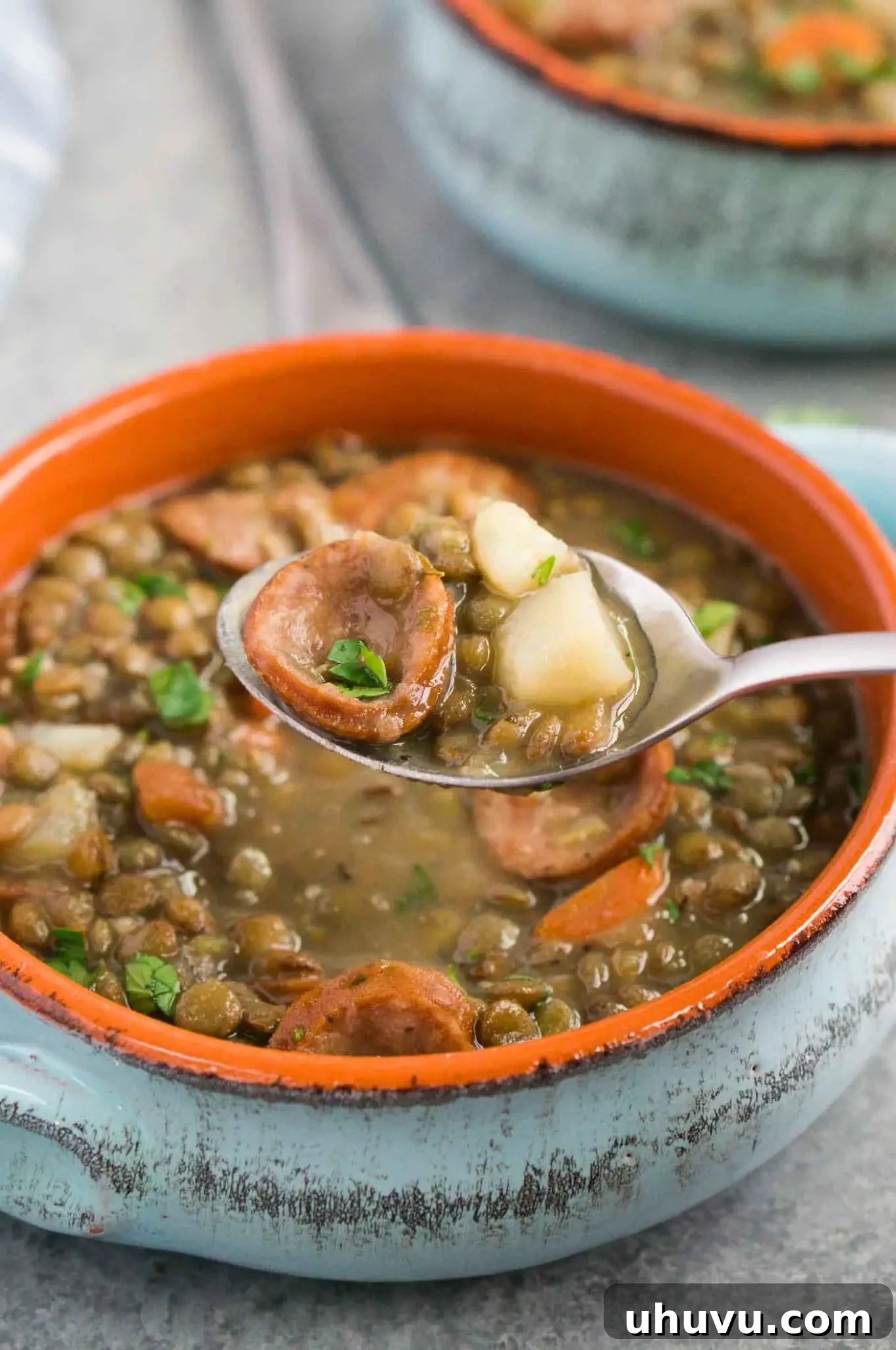 Scooping a spoonful of delicious lentil and sausage soup from a bowl, garnished with fresh parsley.