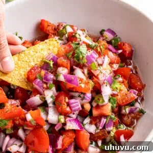close up image of fresh pico de gallo in a white bowl with corn chip