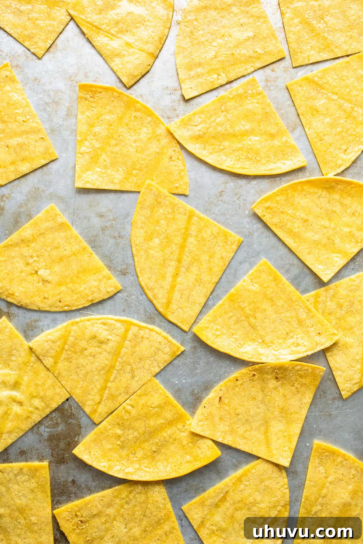 Crispy Oven-Baked Tortilla Chips 6 Cut corn tortilla triangles arranged in a single layer on a baking sheet before baking.