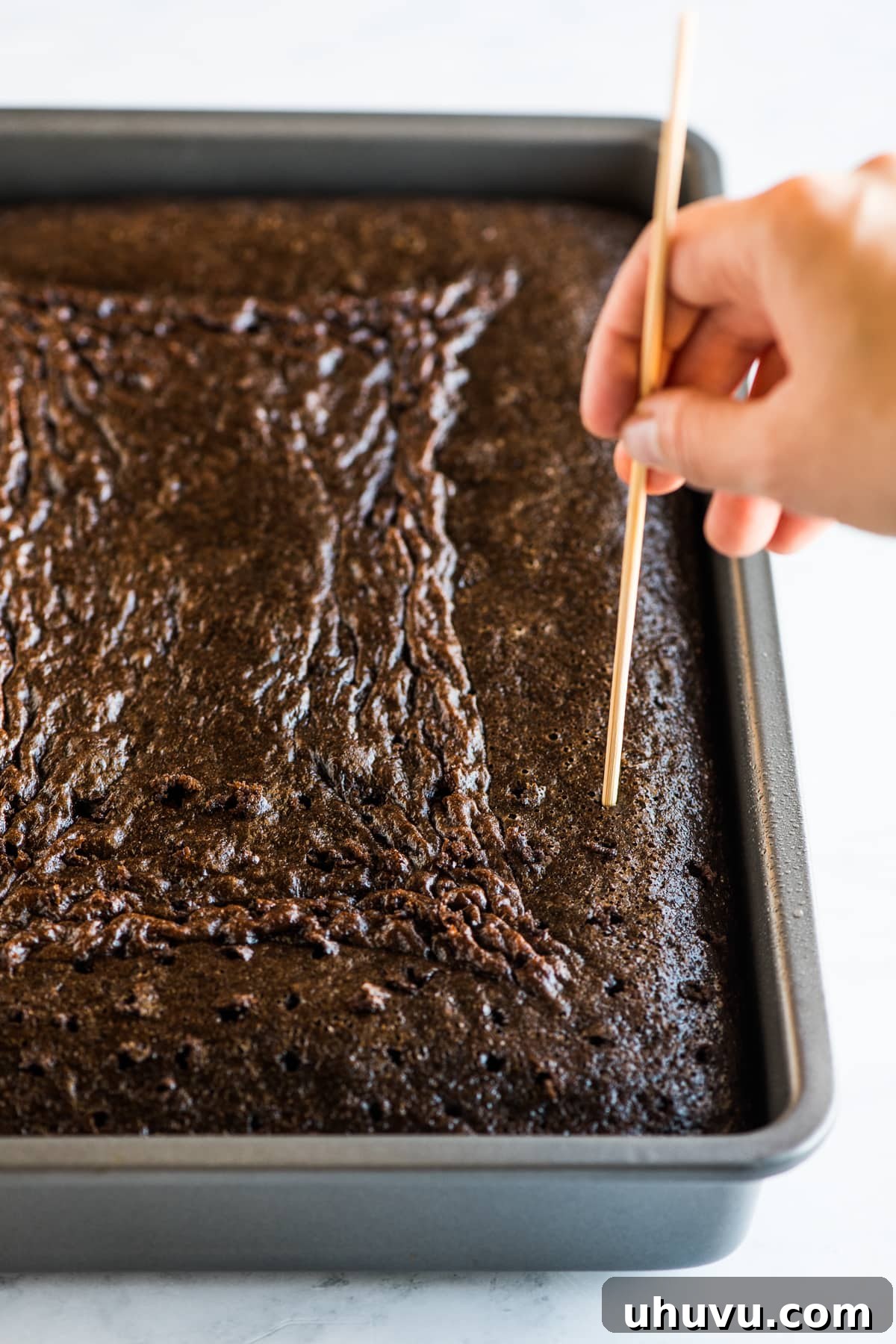 Poking holes into a chocolate tres leches cake with a wooden skewer.