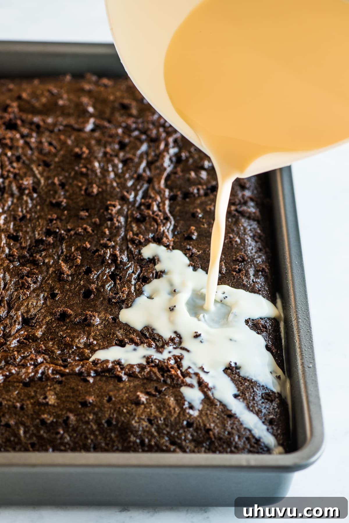 Pouring the three milk mixture over a baked chocolate tres leches cake.