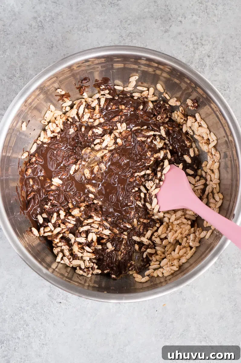 Hand mixing puffed rice cereal, peanut butter, and melted chocolate in a large bowl
