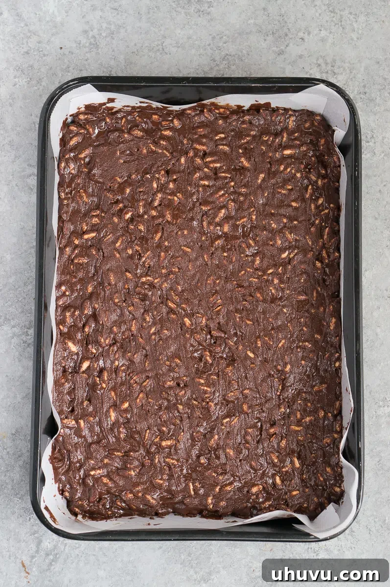 The chocolate crunch mixture spread evenly into a parchment-lined baking pan, ready for freezing