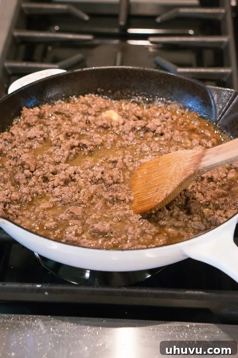 stir fry sauce and cooked broccoli being added to ground beef in a skillet