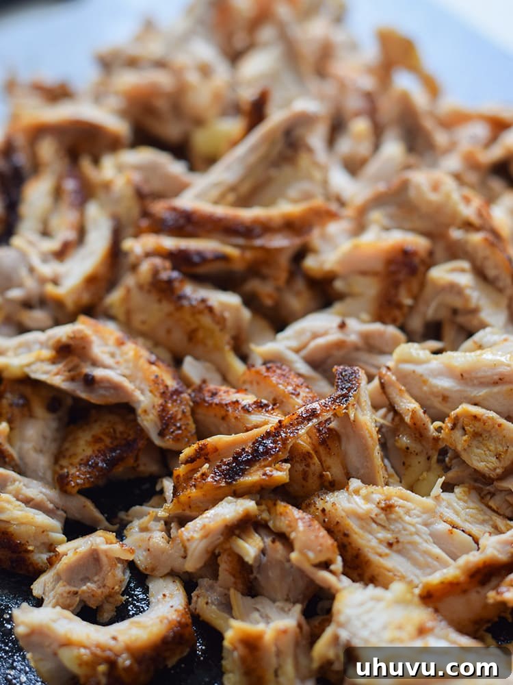 Close-up of a filled corn tortilla, ready to be rolled into a taquito with mashed pinto beans, shredded Mexican cheese, and chili-spiced chicken.