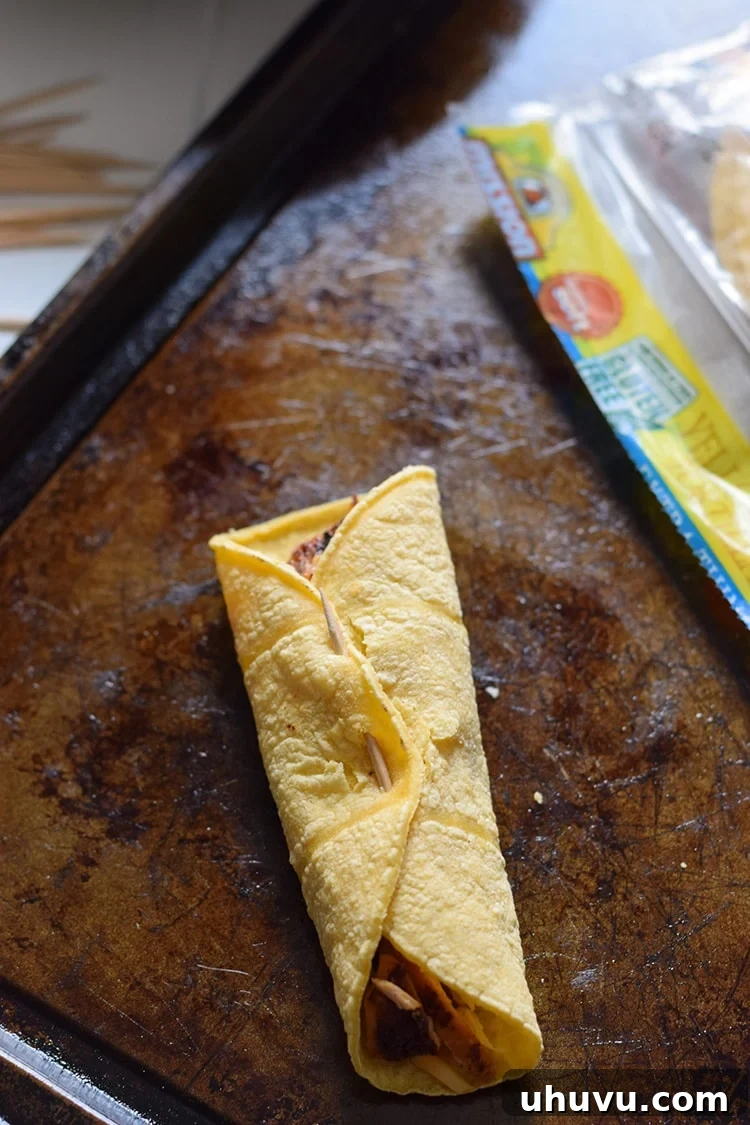 Carefully rolling the filled tortilla tightly to form a taquito.