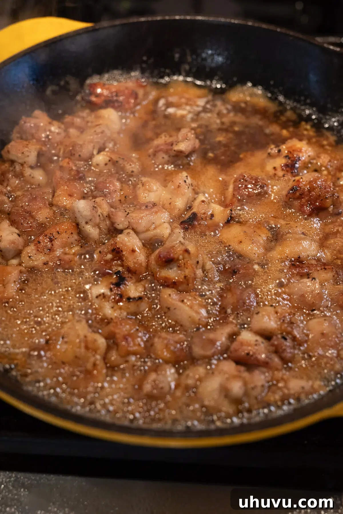 chicken simmering in honey garlic sauce in a skillet to thicken