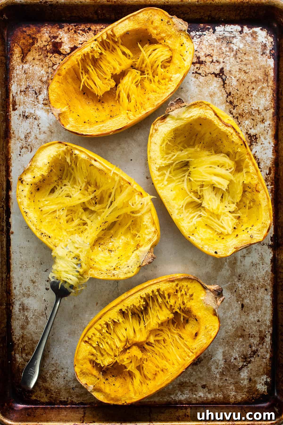 Hearty Spaghetti Squash Bake 5 Stuffed spaghetti squash on a baking sheet scraped into noodles with a fork.