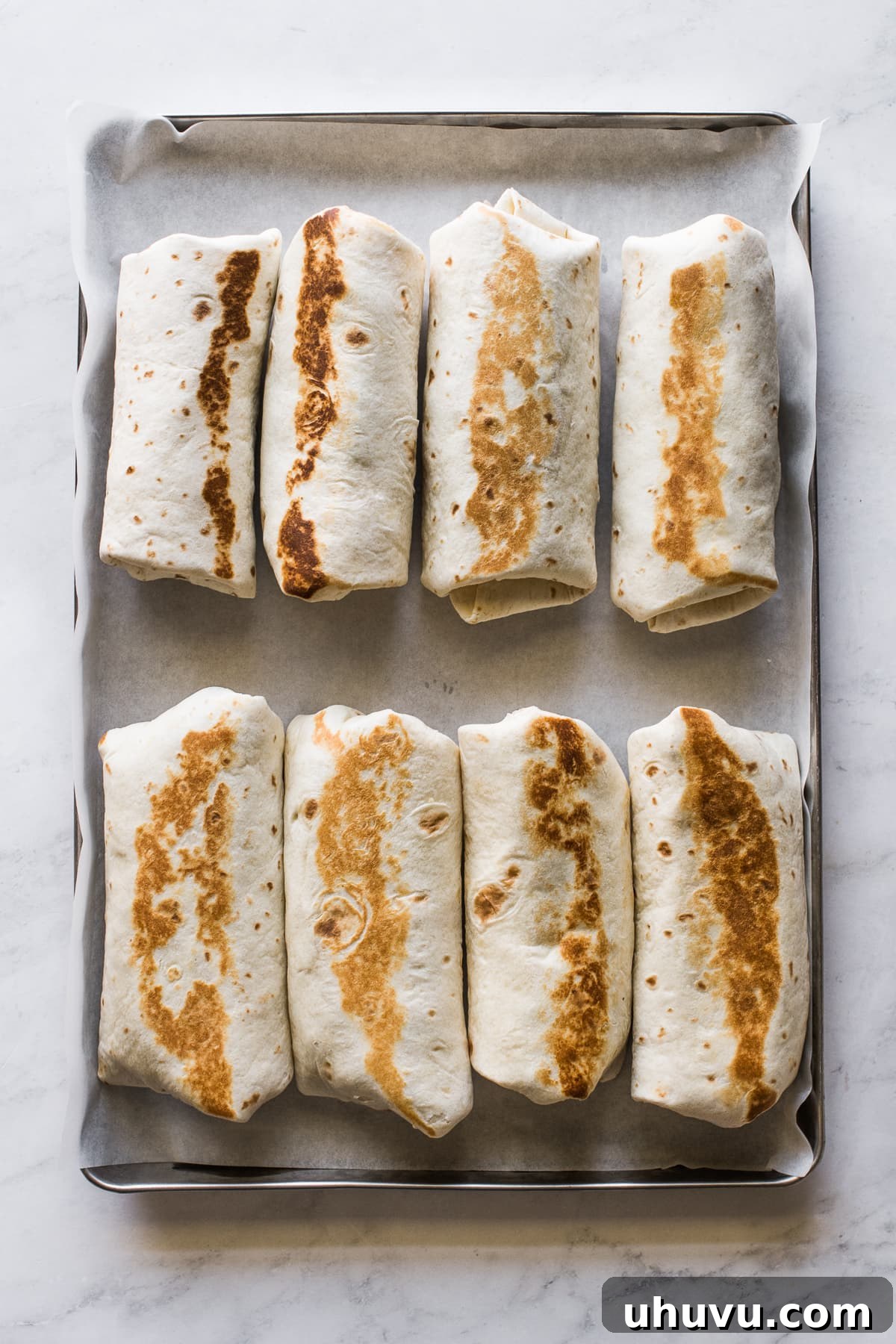 Sunrise Scramble Wraps 4 Rolled and sealed breakfast burritos placed seam-side down on a sheet pan, ready to serve or store.