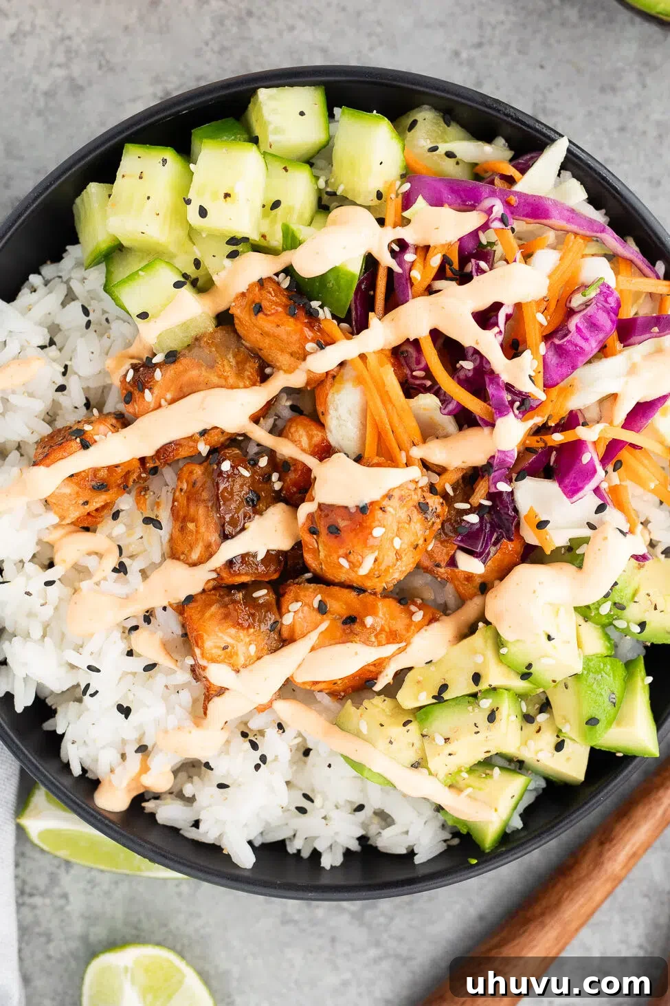 Assembled salmon rice bowl with fluffy rice, tender salmon, fresh cucumbers, creamy avocado, crisp slaw, and a generous drizzle of sriracha mayo, topped with sesame seeds.