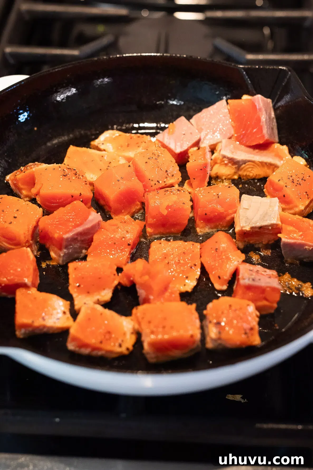 Searing cubed salmon pieces in a hot skillet for a crispy exterior.
