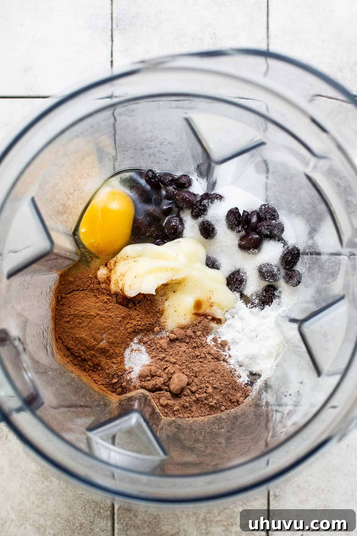 Wholesome Fudgy Black Bean Brownies 4 All the essential ingredients for black bean brownies, including black beans, cocoa powder, ground cinnamon, eggs, melted butter, and baking powder, gathered inside a powerful blender, ready for mixing.