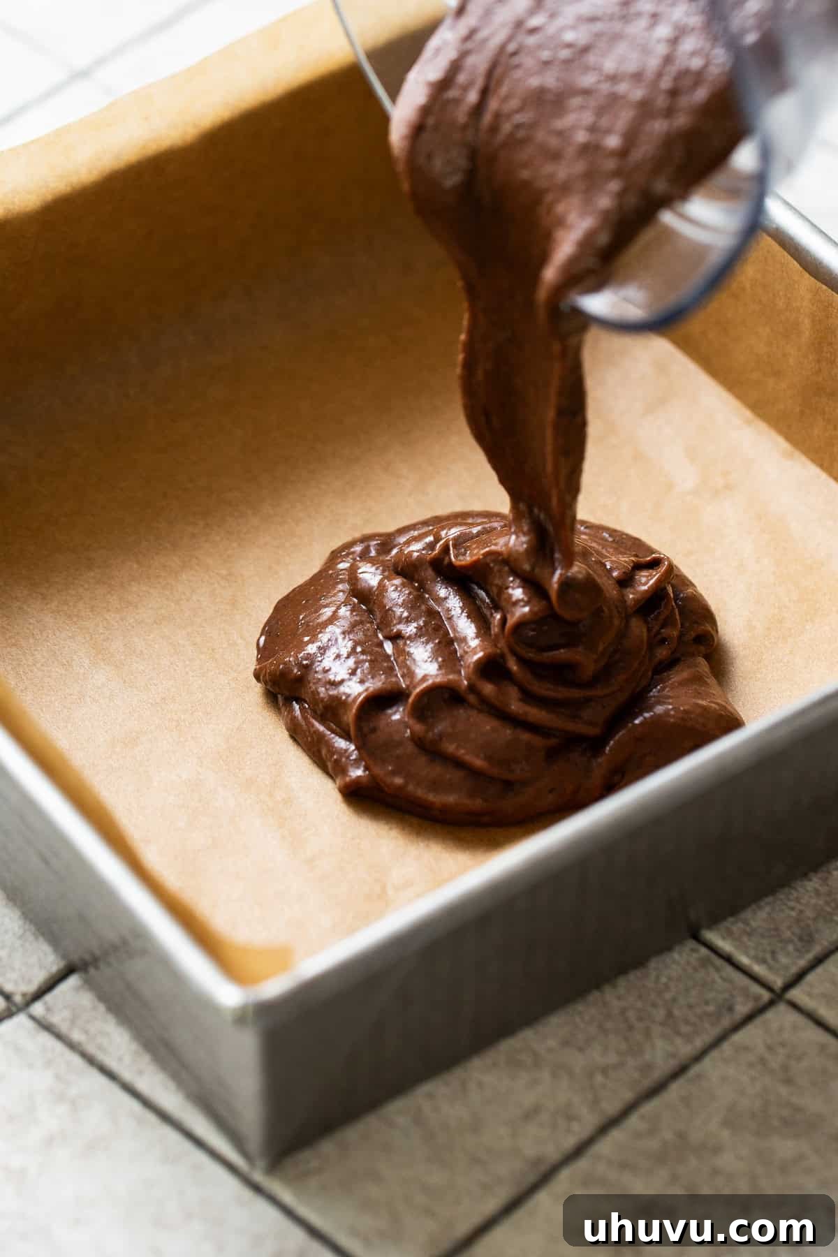 Wholesome Fudgy Black Bean Brownies 6 The luscious batter for black bean brownies being smoothly poured into an 8x8 square baking pan, which is meticulously lined with parchment paper for easy release.
