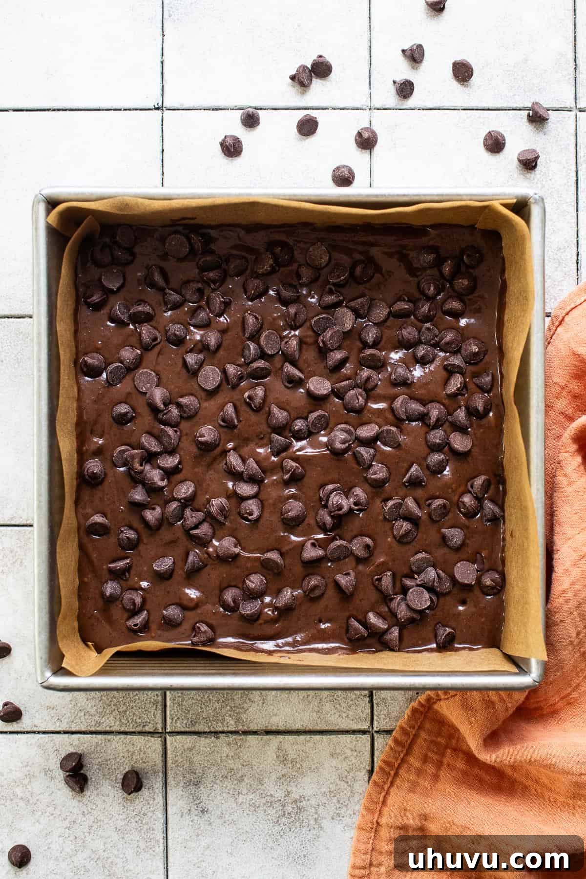 Wholesome Fudgy Black Bean Brownies 7 A close-up view of the rich brownie batter evenly spread in a square baking pan, generously topped with an abundance of semi-sweet chocolate chips, ready for baking.
