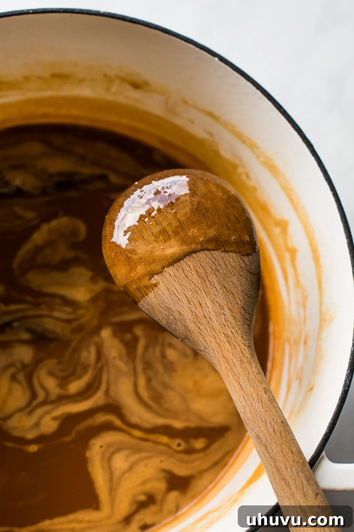 Cajeta sticking to the back of a wooden spoon to show its thickness and consistency. It's a rich amber color.