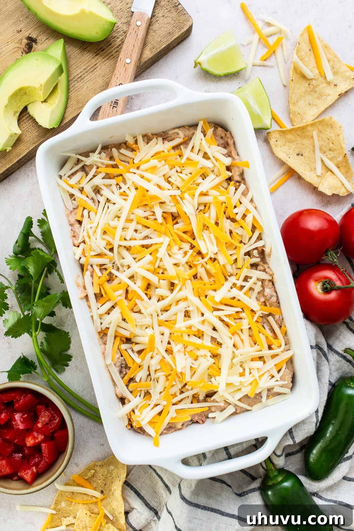 Savory Fiesta Bean Dip 5 An unbaked baking dish filled with bean dip, generously topped with a layer of shredded cheese, poised and ready to be placed into the oven for melting and bubbling perfection.