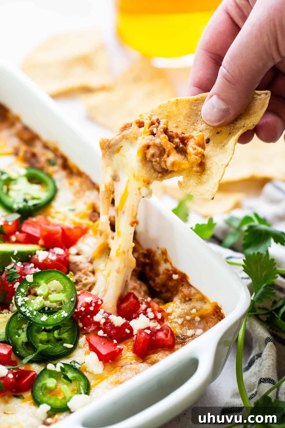 Savory Fiesta Bean Dip 7 A close-up of a tortilla chip, generously loaded with warm, melted cheese and creamy bean dip, pulled tantalizingly from the baking dish, showcasing the inviting stretch of cheese.
