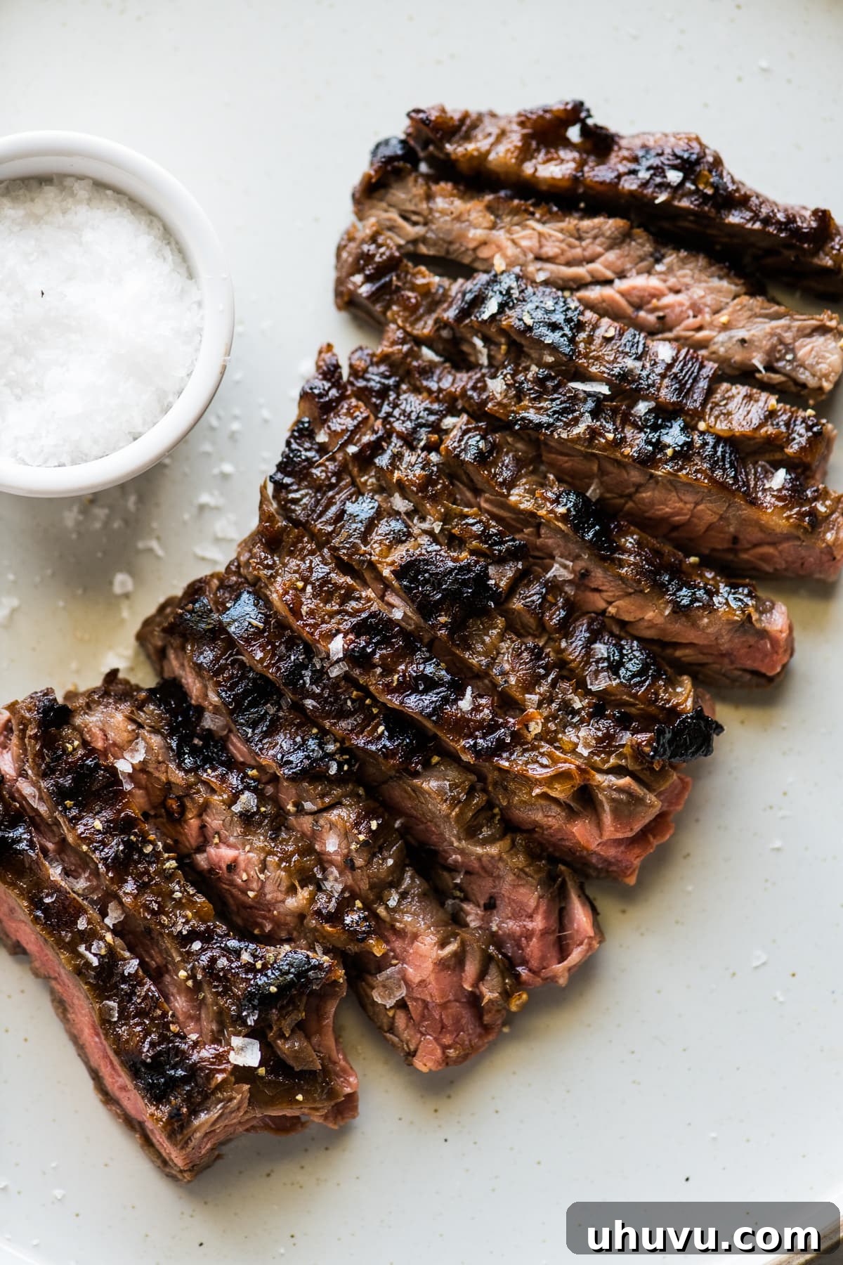 Skirt Steak Flavor Boost 2 Sliced grilled skirt steak sprinkled with flaky sea salt on a white plate.