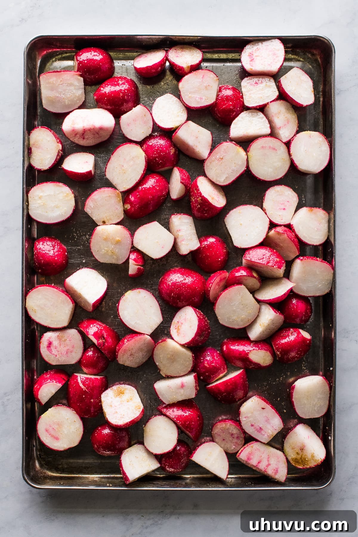 Radishes tossed with olive oil and spices on a sheet pan, ready for roasting.
