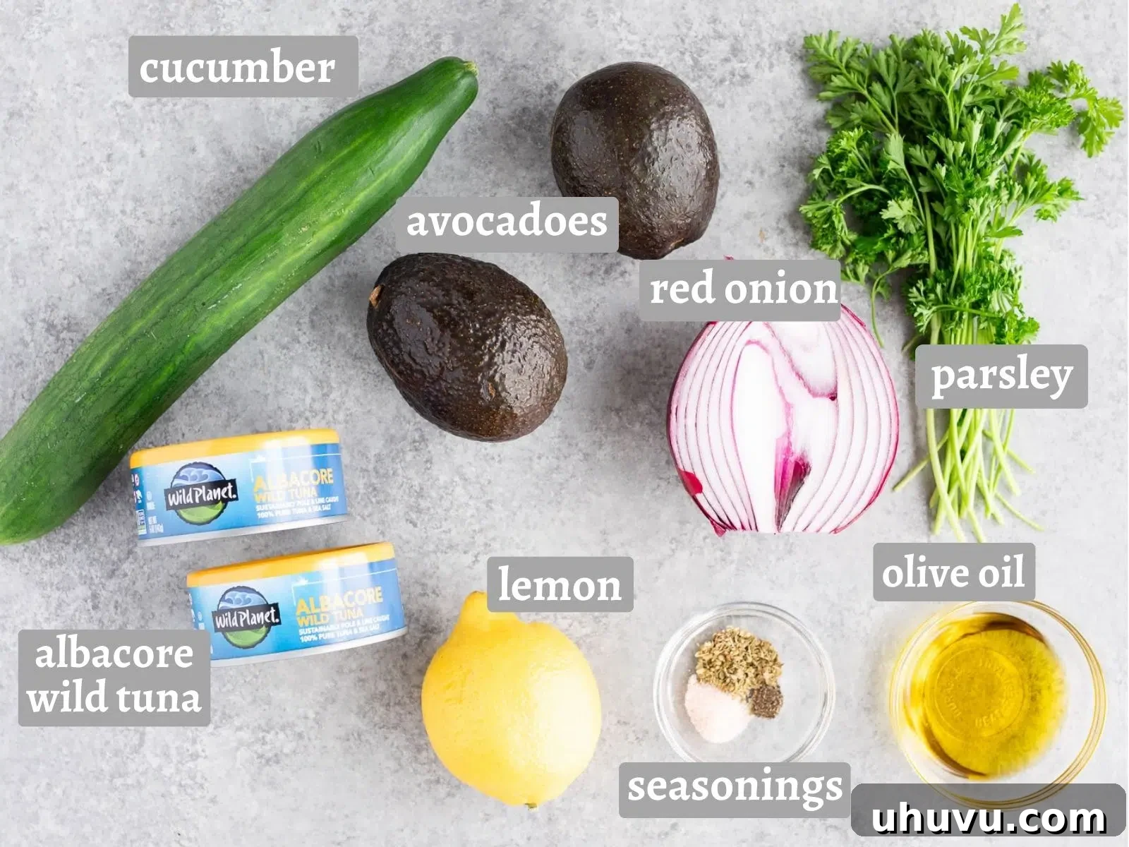 Fresh ingredients for avocado tuna salad: whole avocados, sliced cucumber, canned tuna, red onion, and parsley.
