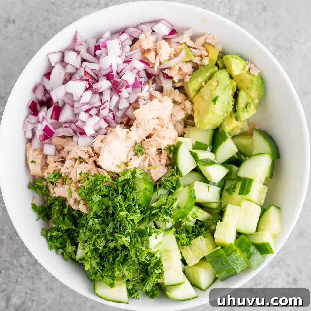 A bowl filled with cubed avocado, chopped cucumber, flaked tuna, and red onion, awaiting dressing.