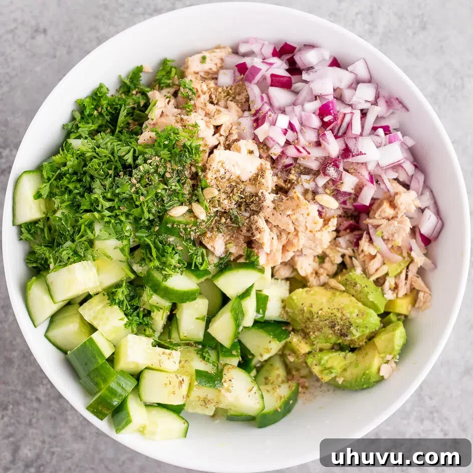 A hand drizzling lemon-olive oil dressing over the avocado tuna salad ingredients in a bowl.