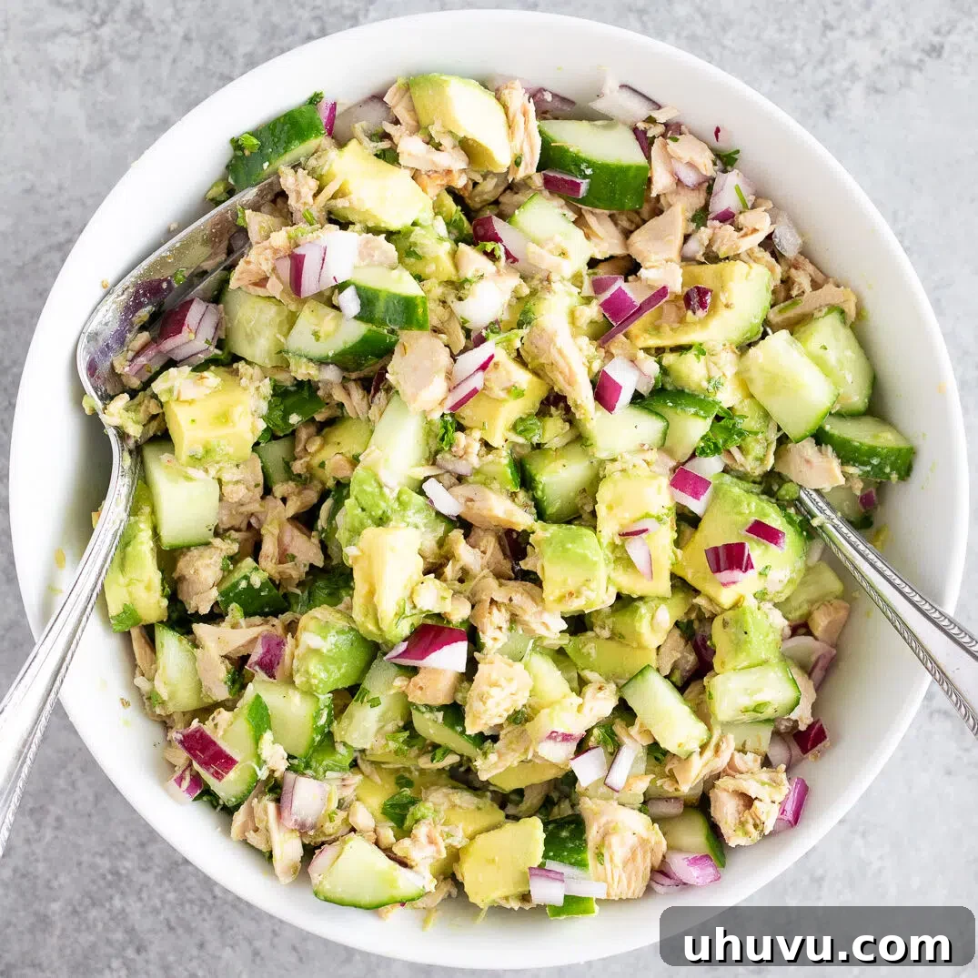 A close-up shot of the avocado tuna salad being gently tossed with the dressing.