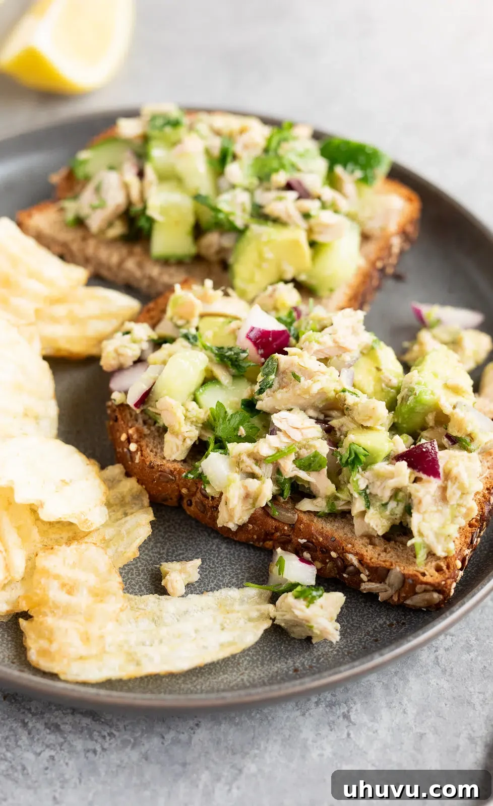 Avocado tuna salad artfully arranged on a piece of toasted bread, accompanied by a small bowl of chips.