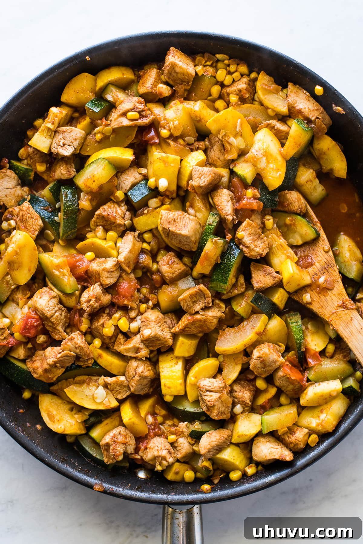 Cooking chicken and squash in a skillet with a wooden spoon.