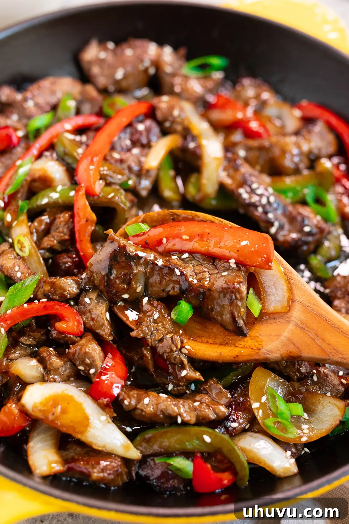 Scooping a serving of beef and peppers stir fry from a skillet