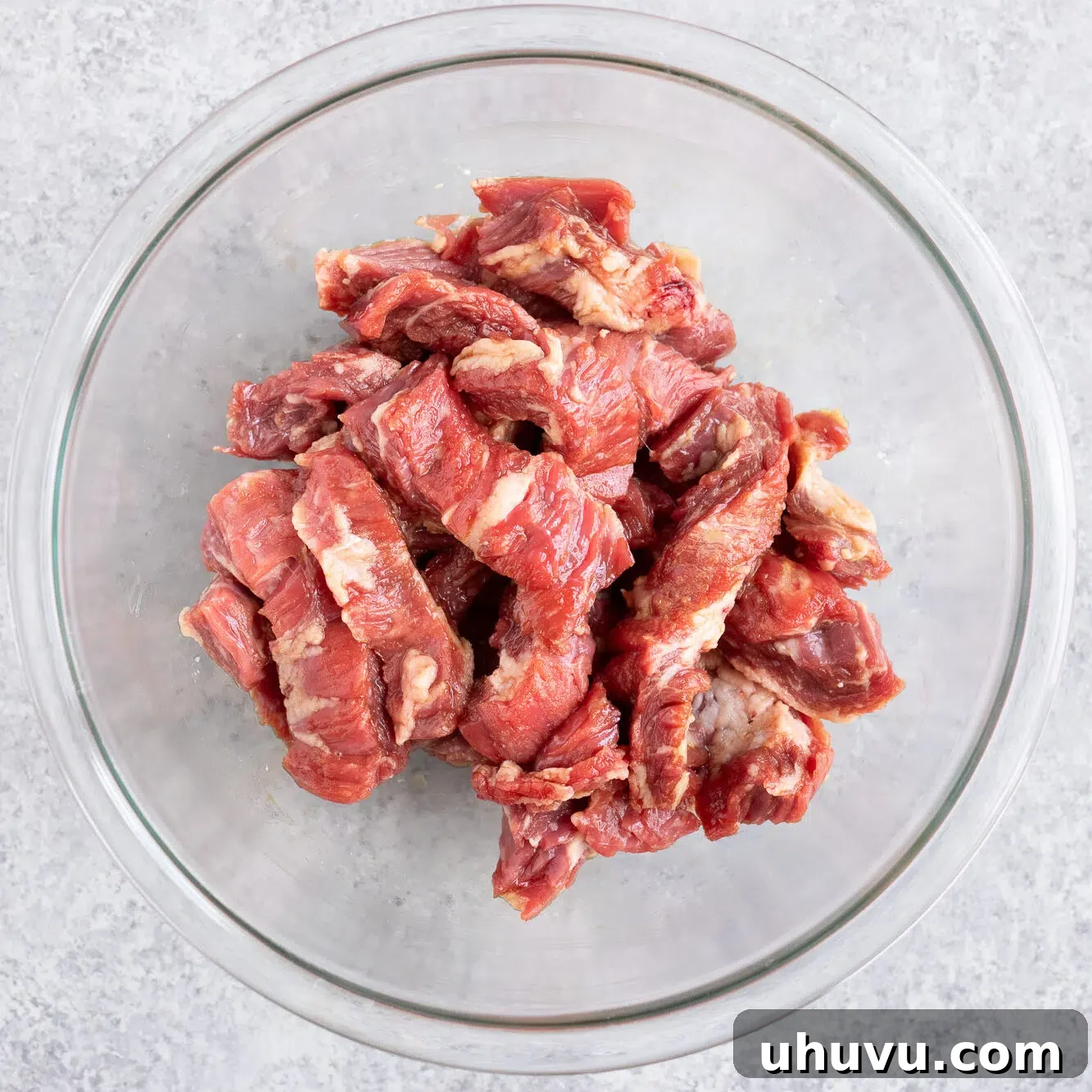 Sliced flank steak marinating in a bowl with soy sauce and cornstarch