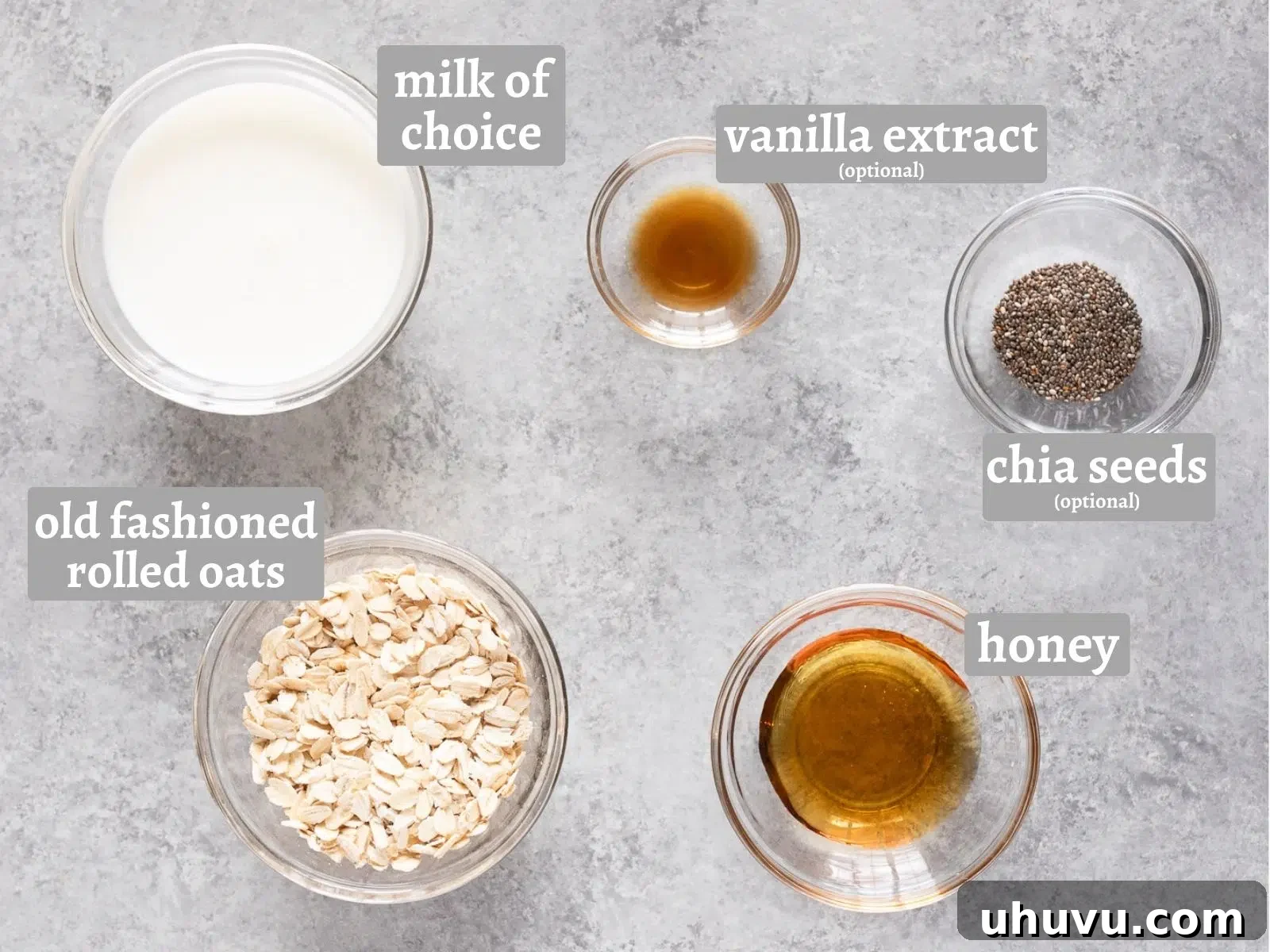 A flat lay of ingredients laid out for making overnight oats, including a bowl of rolled oats, a glass of milk, a jar of honey, vanilla extract, and a small dish of chia seeds.