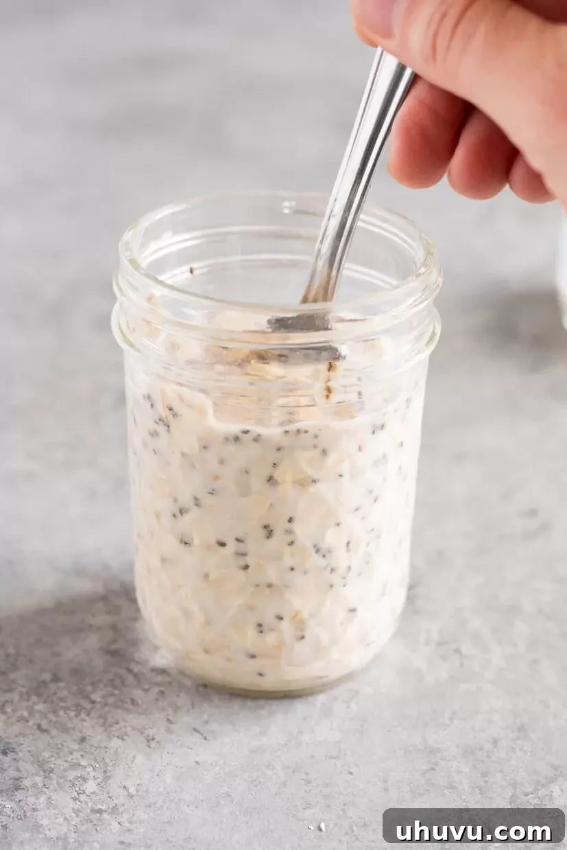 A spoon stirring the mixture of oats, milk, and other ingredients vigorously in a glass jar, ensuring everything is well combined.