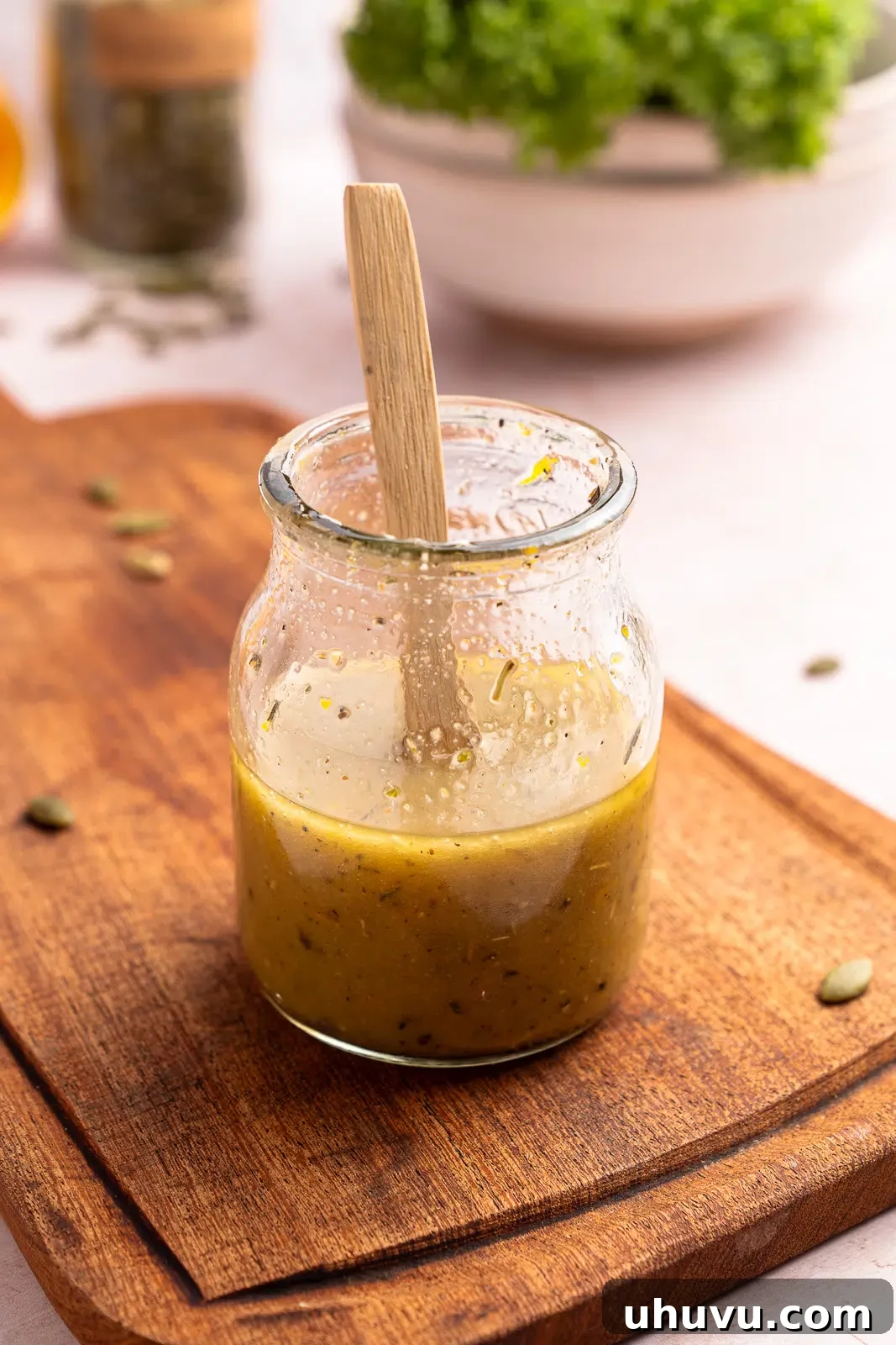 Close-up of a hand stirring red wine vinaigrette in a clear glass bowl, showcasing its emulsified texture
