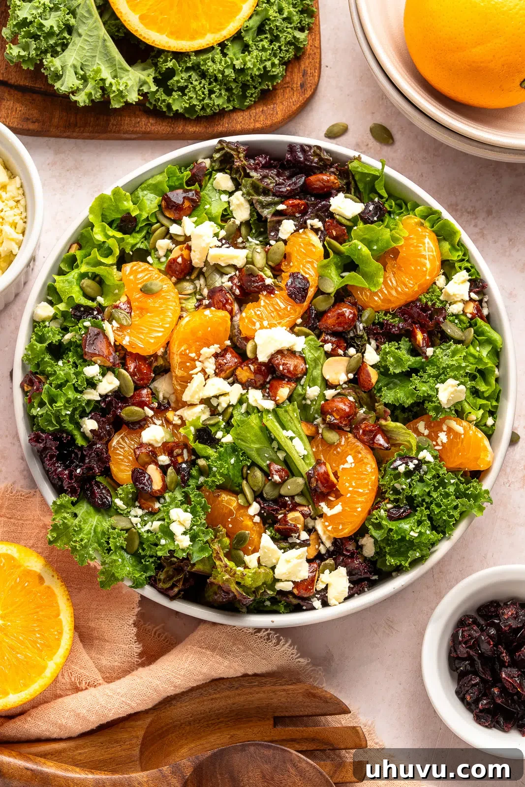 Overhead shot of a large white bowl with mixed greens, clementines, dried cranberries, and feta cheese, ready for dressing
