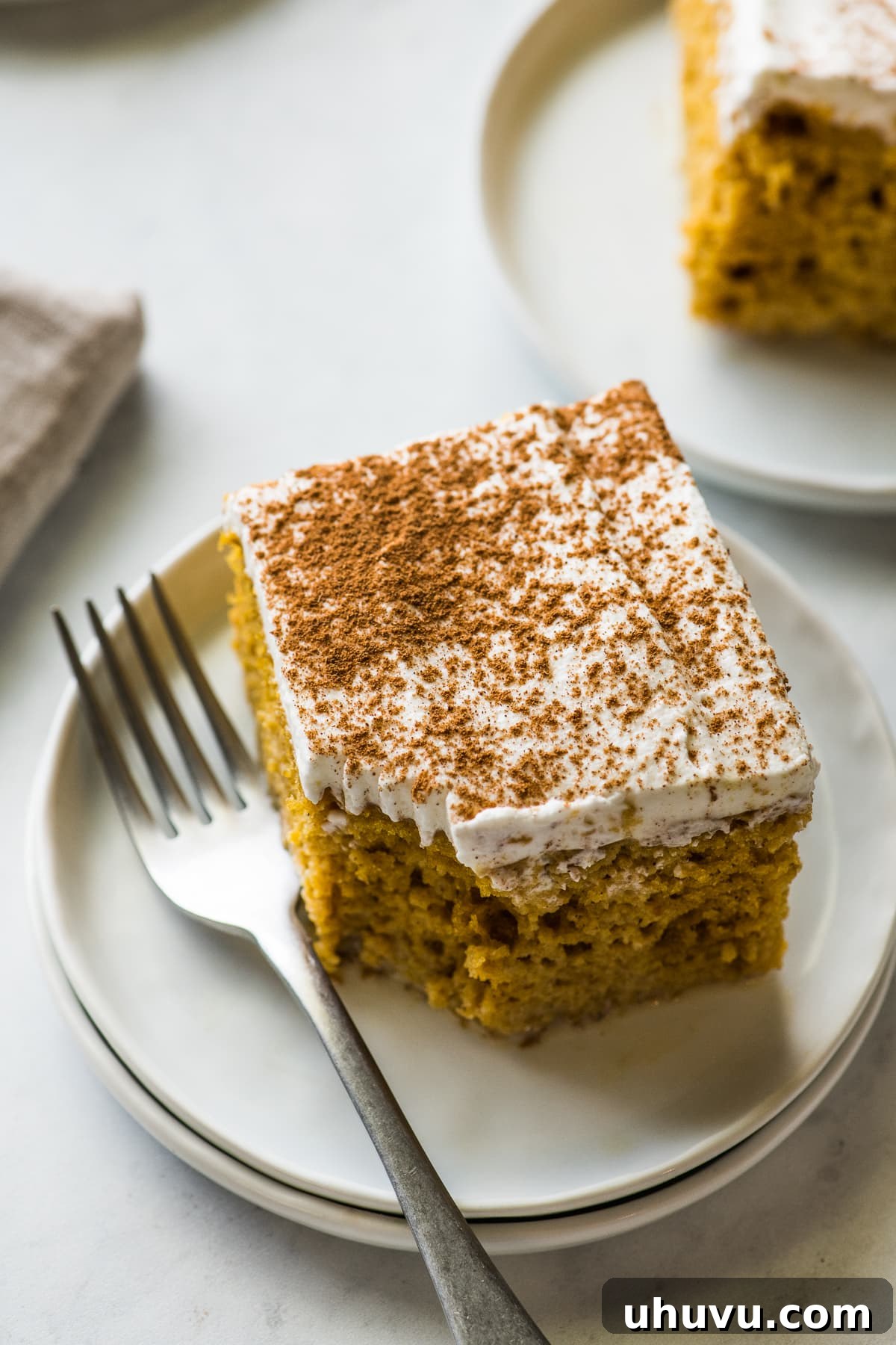 A delectable slice of pumpkin tres leches cake with a bite taken out, showing its moist interior and creamy topping.