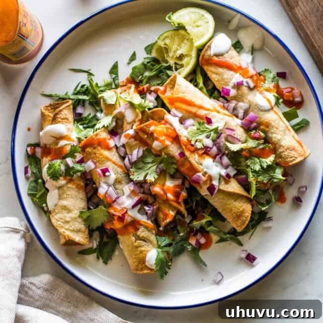 Air fryer chicken taquitos on a plate with lettuce and topped with sour cream, cilantro, salsa, and diced onions.